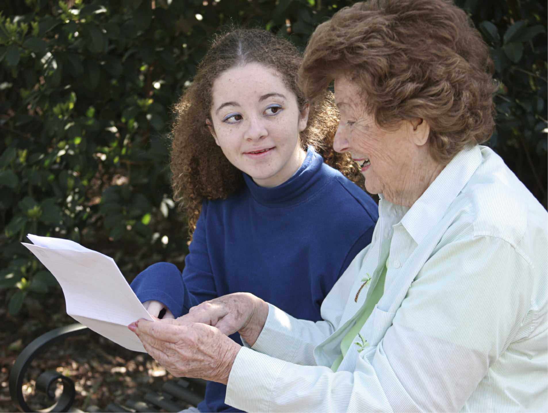 Older and younger women reading a document near hedge